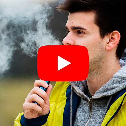 Jovem utilizando cigarro eletrônico ao ar livre, com fumaça visível ao redor do rosto.